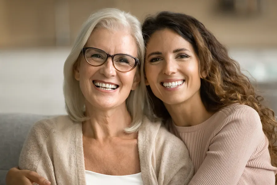 A mother and her grown daughter smiling together